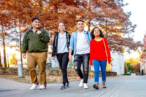 four students walking together on campus, fall trees in the background