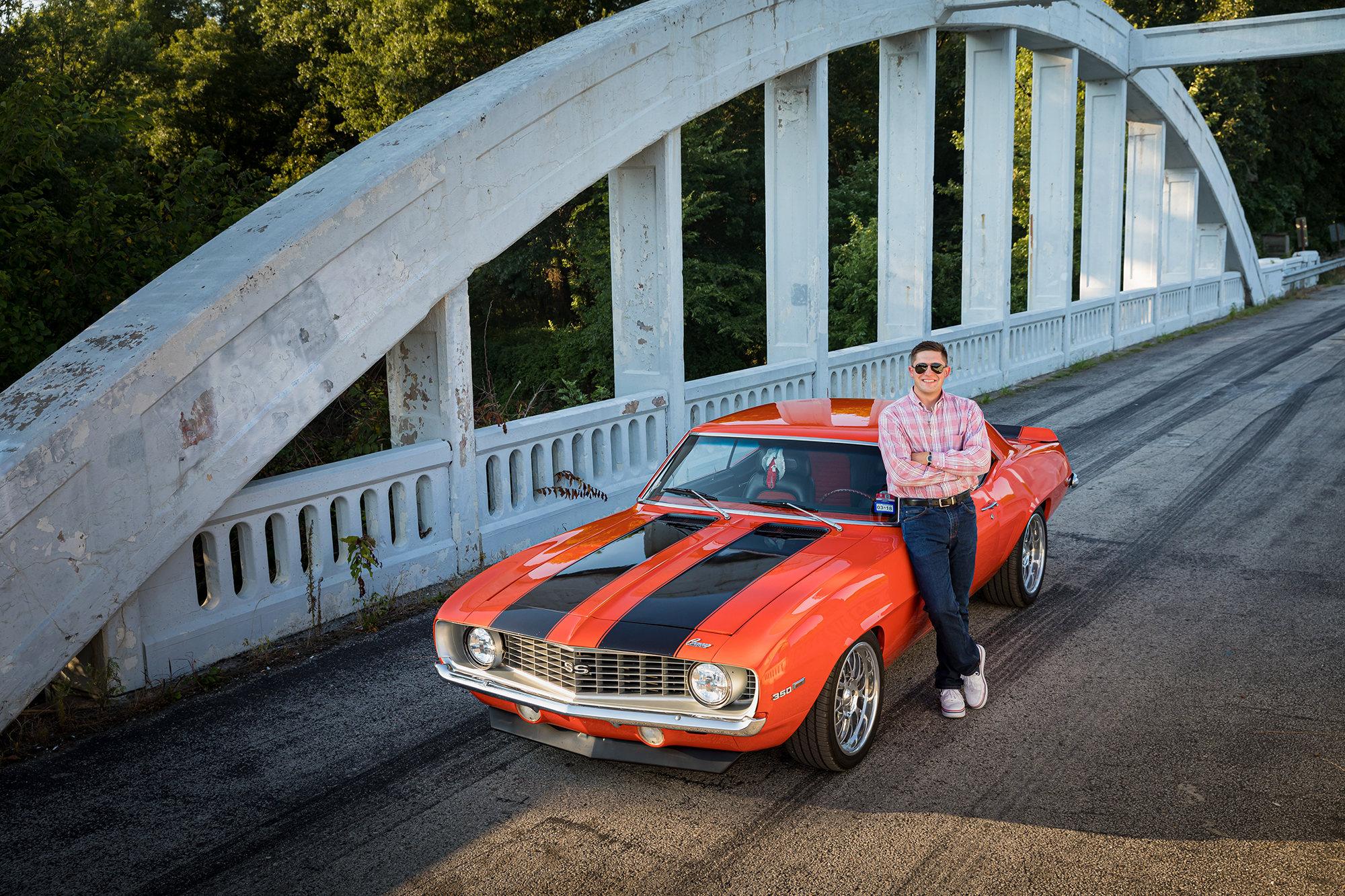 Nick Broadbent standing against muscle car on bridge. Photo Credit: Russell Cothren